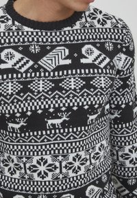 Schwarz-weißer Strickpullover mit einem Fair Isle-Muster, das Rentiere, Schneeflocken und Handschuhe zeigt, runder Halsauschnitt und gerippte Bündchen.