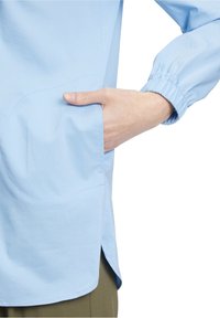 Jasnoniebieska, długa koszula z długim rękawem, z elastycznymi mankietami, boczną kieszenią i lekko zaokrąglonym dołem. Gładki materiał o matowym wykończeniu.