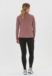 Långärmad, mauve idrottstopp med texturerade detaljer, matchad med svarta leggings och lätta löparskor. Bakifrån.