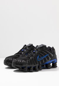 Sorte Nike sneakers har en struktureret mesh-overdel med blå detaljer og en kraftig sål med synlige luftstøddæmpningssegmenter.