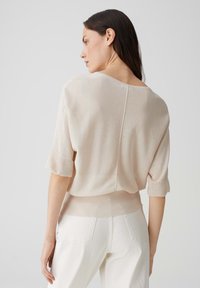 Hellbeiger, kurz geschnittener Pullover mit kurzen, umgeschlagenen Ärmeln, weicher Textur, Rückennähten, kombiniert mit weißen, hoch taillierten Hosen.