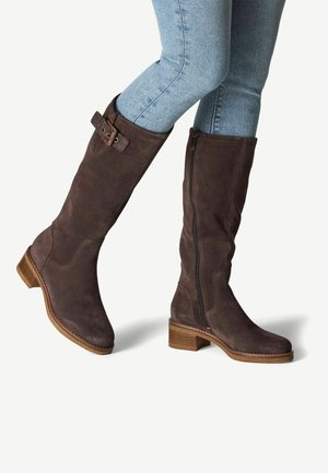 Bottines marron en daim jusqu'au genou avec une fermeture éclair sur le côté et un détail de boucle, dotées d'un talon en bois empilé et d'une texture lisse.