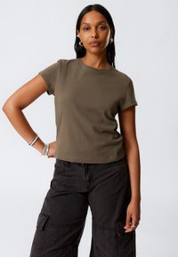 T-shirt din bumbac de culoare verde măslin, cu mâneci scurte și guler rotund, având un croi scurt, asociat cu pantaloni cargo negri, care au buzunare laterale.