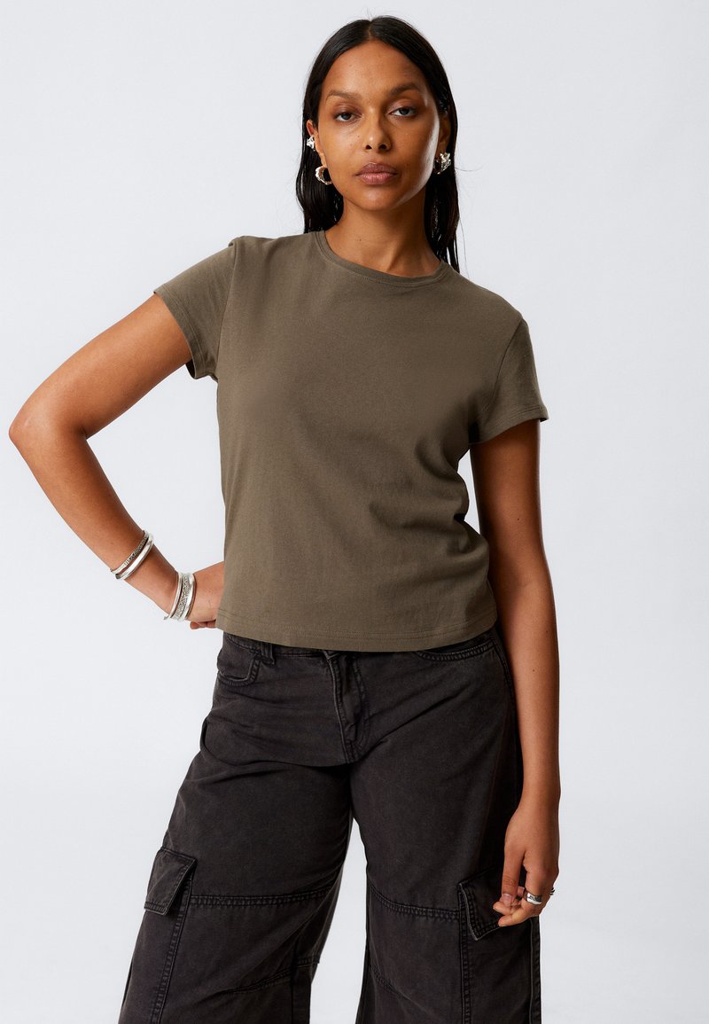 T-shirt din bumbac de culoare verde măslin, cu mâneci scurte și guler rotund, având un croi scurt, asociat cu pantaloni cargo negri, care au buzunare laterale.