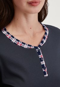 Dunkelblaues Oberteil mit kariertem Kragen, der rote Blumen zeigt, drei dekorative Knöpfe und kurze Ärmel hat. Glatte Stoffstruktur.