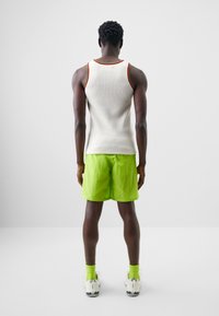 Hvit ribbet tank topp med rød og gul kant, sammen med lysegrønne shorts, matchende grønne sokker og teksturerte hvite joggesko.