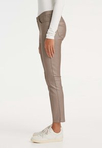 Pantalons slim en beige métallique avec une texture lisse, dotés d'une fermeture à un bouton et de poches latérales, associés à des baskets blanches.