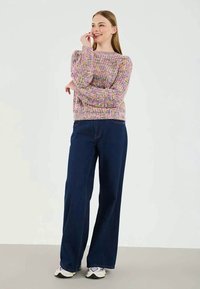 Multicolored knitted sweater with puffed sleeves, paired with high-waisted, wide-leg dark denim jeans and white sneakers.