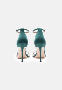 Tyrkysové saténové sandály na vysokém podpatku s pásky kolem kotníku a špičatou špičkou. Obsahují tenké stiletto podpatky a klenotové akcenty na přední straně.