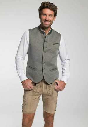Grahamuster-Weste in Grau mit grünen Akzenten, fünf Knöpfen und zwei Taschen, kombiniert mit hellbraunen Leder-Shorts mit floralen Stickereien und Knöpfen.