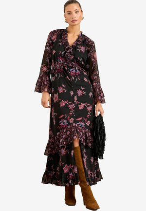 Abito maxi nero floreale con maniche e orlo a volant, caratterizzato da motivi rosa e blu. Abbinato a stivali marroni fino al ginocchio e una borsa nera.