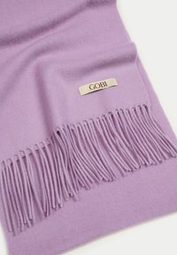 Lila scarf i mjukt tyg med fransade kanter och en märkesetikett. Slät textur med en subtil glans.