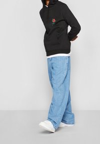 Černá mikina s kapucí s výšivkou růže, klokánek kapsa, doplněná světle modrými volnými džínami a bílými teniskami. Jednoduchý design a pohodlný střih.