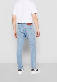 Světle modré džínové kalhoty s volnějším střihem, s hnědým koženým štítkem na zadním pásku a dvěma zadními kapsami. Nošeny s bílými teniskami.