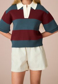 Dzianinowy top w bordowo-turkusowe paski, z dużym białym kołnierzem i prążkowanym dołem. Do tego białe szorty w paski.