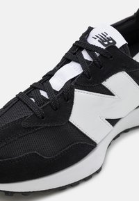 Nahaufnahme eines schwarz-weißen Sneakers, der strukturierten Stoff, Wildleder-Überzüge, dicke schwarze Schnürsenkel sowie ein markantes weißes Logo an der Seite und eine gepolsterte Zunge zeigt.