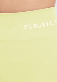 Limegroene geribbelde tailleband met de tekst "SMIL" in het wit. Gladde textuur, lichte rek, ontworpen voor actieve kleding. Eenvoudig en functioneel ontwerp.