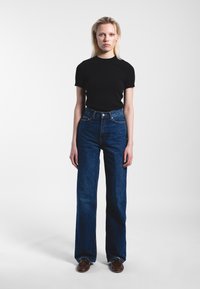 High-waisted blue denim jeans with a wide-leg cut, paired with a fitted black t-shirt, both displayed against a plain backdrop.