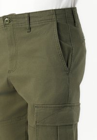 Olive green cargo pants made of cotton blend fabric, featuring front pockets and side cargo pockets with stitched accents and a button closure.