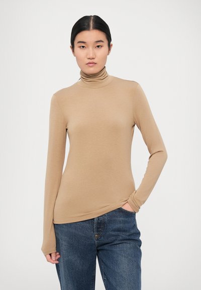 Pikad varrukad, beežist turtleneck, mis on valmistatud siledast kangast. Omab vormitud disaini ja kogutud detaili vöökohal, millele on lisatud tumehallid teksad.