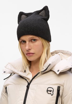 Black ribbed knit hat with mesh cat ears. Worn with a beige puffer jacket featuring a zippered front and logo patch.