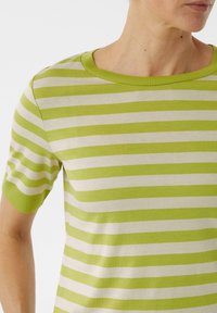 Zielona i kremowa koszulka w paski z krótkimi rękawami, okrągłym dekoltem i miękkim, teksturowanym materiałem. Paski są równomiernie rozmieszczone.