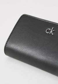 Black leather wallet with pebbled texture, featuring a silver "ck" logo on the front, and clean stitched edges.
