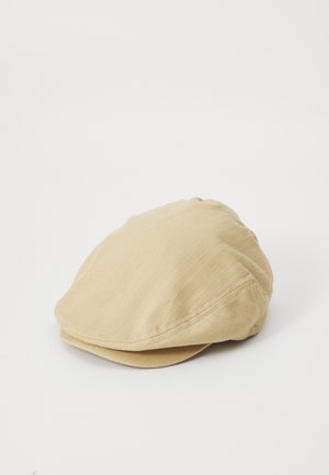 Casquette plate beige avec un motif chevrons subtil, tissu doux et visière courbée, posée sur un fond blanc.