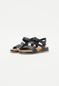 Black leather sandals with cross straps, open toe, cushioned footbed, and low platform sole. Smooth texture and minimalistic design.