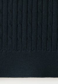 Gros plan d’un tissu tricoté bleu marine foncé avec un motif à torsades verticales et un ourlet côtelé en bas.