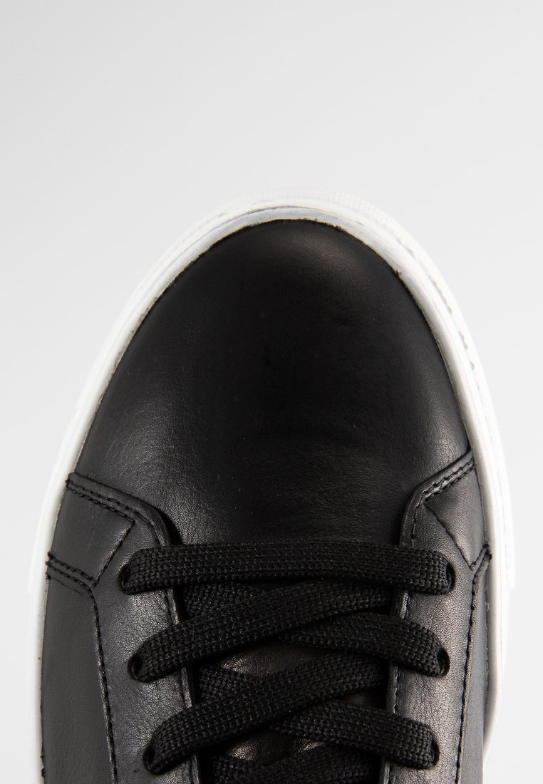 Schwarze Ledersneaker mit weißer Gummisohle. Besitzt schwarze Schnürsenkel und eine strukturierte Oberfläche, die das glatte Material und das schlichte Design hervorhebt.
