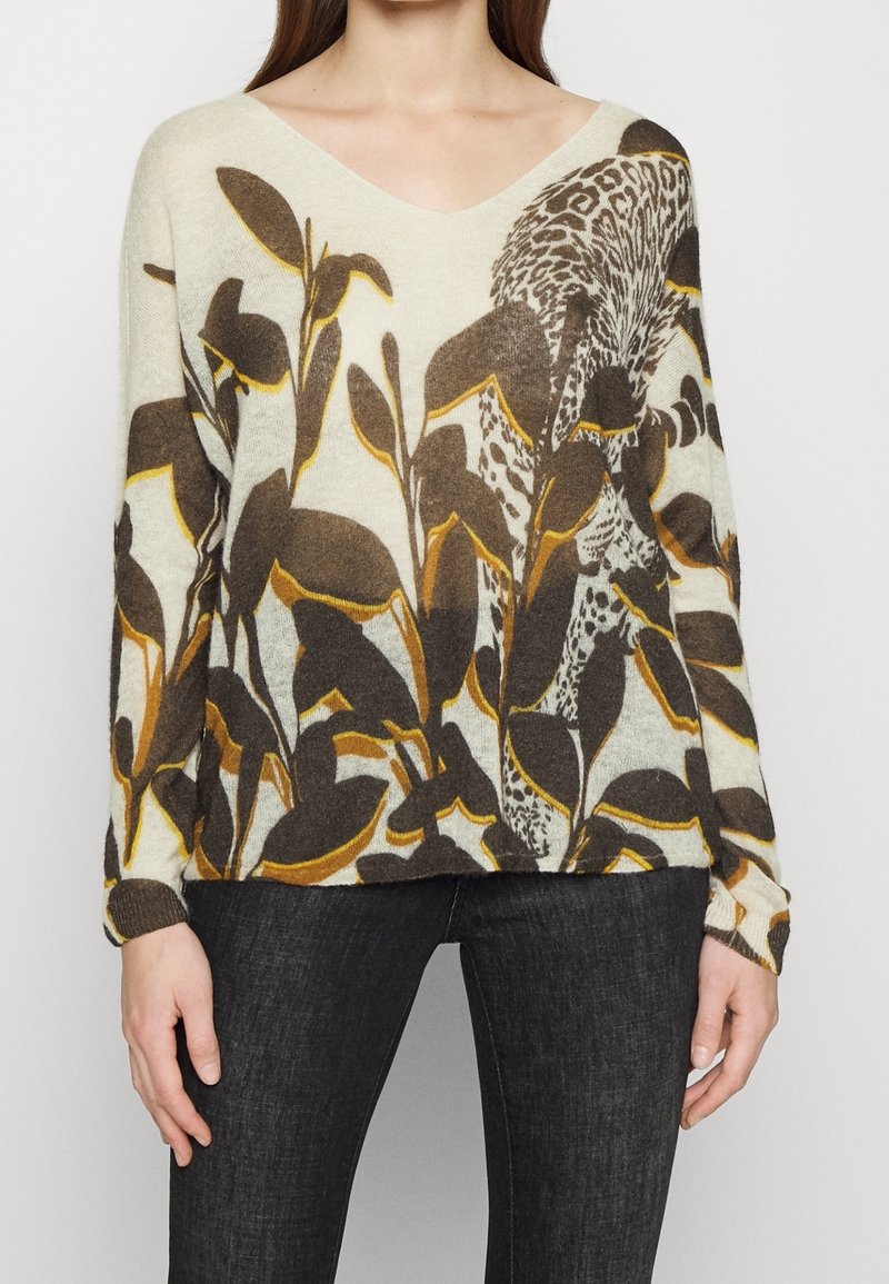V-Ausschnitt Pullover in Creme mit braunen und gelben Blattmustern. Weiche Textur, lockere Passform, lange Ärmel und gerippte Bündchen.