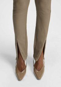 Beige tailored pants with side slits, made from smooth fabric. Paired with pointed toe, glossy beige heels.