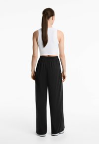 Weißes Croptop mit hohem Kragen und ärmellosem Design, kombiniert mit schwarzen weit geschnittenen Hosen mit elastischem Bund und weicher Textur.