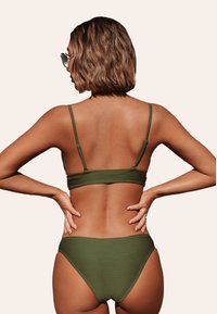 Bikini verde oliva a coste con spalline sottili e design senza cuciture. La parte superiore ha un morbido elastico, mentre la parte inferiore ha un taglio a vita media.