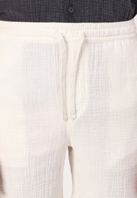 Pantalons de jogging couleur crème en tissu texturé, avec une taille élastique et un cordon de serrage. Comprend des poches latérales et une coupe décontractée.