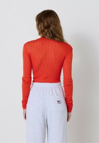 Persona, kura skatās prom, ģērbusies sarkanā, garajā piedurknē, ar punktiņiem un gaiši pelēkās sporta biksēs ar mazu krāsainu logotipu aizmugurējā kabatā.