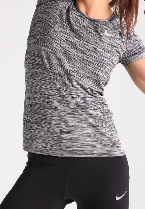 Camiseta deportiva de manga corta en tejido negro y gris jaspeado, con un cuello redondo y el logo de Nike en el pecho. Combinada con leggins negros.