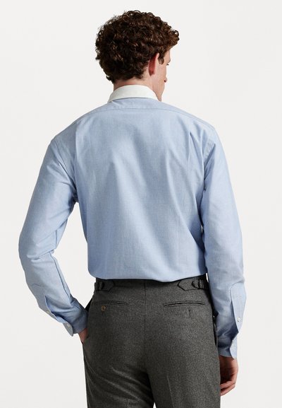 Lyseblå skjorte med lange ermer og hvit krage, kombinert med grå teksturerte bukser med baklommer og justerbare stropper.