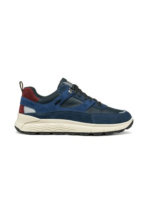 Zapatilla de ante azul y gris oscuro con acento en el talón en color marrón, cordones negros con patrón, suela gruesa beige y suela exterior de goma negra.