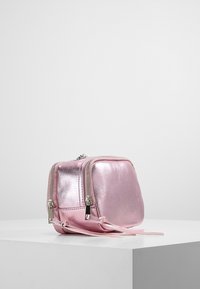 Zaino metallico rosa con forma rettangolare, dotato di due scomparti con zip e una superficie liscia e lucida. Include una tracolla regolabile.