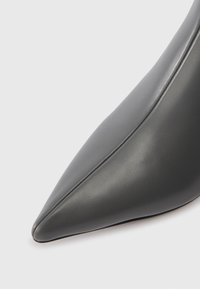 Norādīta purna daļa eleganta tumši pelēka ādas augstpapēžu kurpe ar redzamām šuvēm augšējā šuvē uz baltā fona.