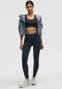 Sujetador deportivo negro, chaqueta gris con cremallera y leggins oscuros de entrenamiento. Tejido texturizado, diseño de cintura alta, combinados con zapatillas deportivas ligeras.