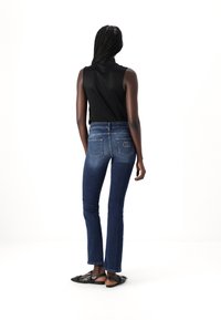 Jeans de mezclilla azul oscuro con corte recto, que cuentan con dos bolsillos traseros y un discreto detalle de logo. Combinados con una blusa sin mangas negra y sandalias.