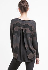 Schwarzer und brauner Camouflage-Muster-Pullover mit lockerer Passform, der einen tiefen Rückenausschnitt und strukturierten Stoff aufweist. Lange Ärmel und gerippte Bündchen.