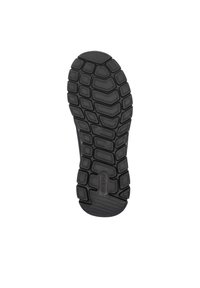 Black rubber shoe sole with textured traction pattern, featuring rounded shapes and ridges for grip. Includes prominent brand logo.