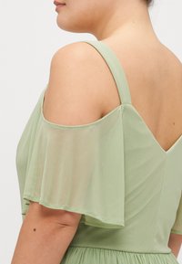 Lichtgroen jurk met korte, doorzichtige mouwen en een diepe V-achterkant. De stof lijkt glad met een vloeiende uitstraling, waarin een tekstuurpatroon te zien is.