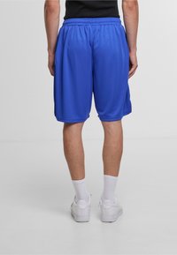 Blå træningsshorts lavet af letvægtigt stof, med elastisk talje, sidelommer og en løs pasform. Båret med hvide sneakers.