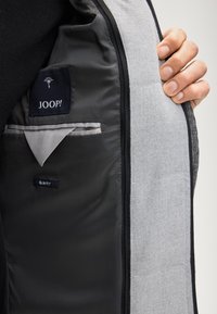 Wnętrze szarej kurtki wykończone jest czarną podszewką z metką "JOOP!" i kieszonką, uzupełnione o szarą, materiałową powłokę z etykietą slim fit.