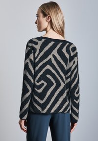 Maglione lavorato a maglia con un motivo a zigzag in bianco e nero ad alto contrasto, colletto rotondo e vestibilità comoda. Tessuto morbido con maniche lunghe.
